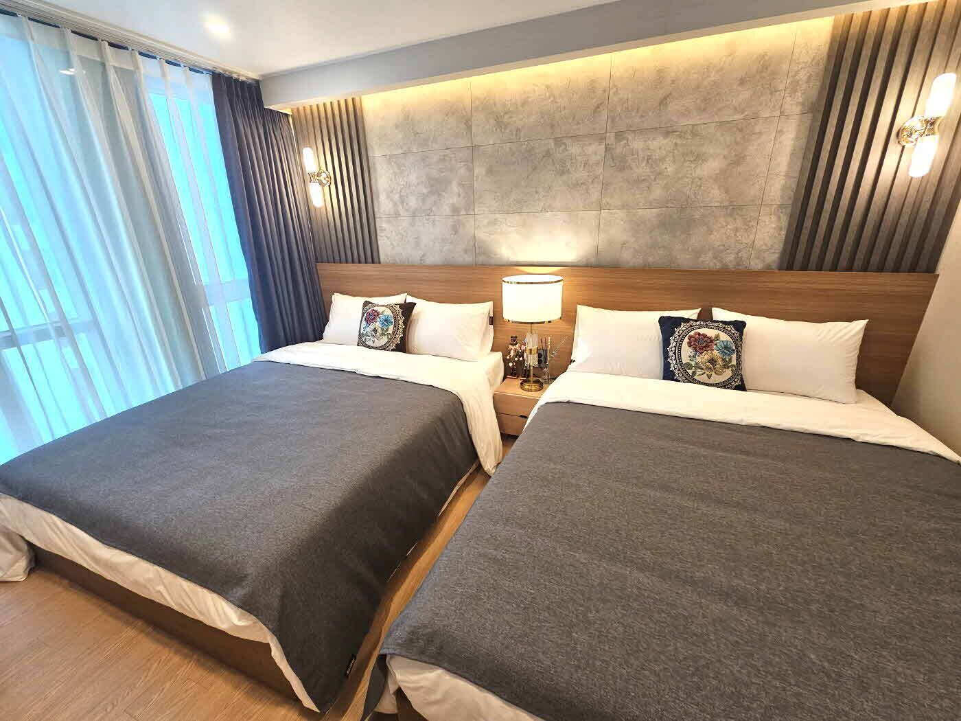 Habitación con cama doble, ventana grande, cabecero de madera y mesita de noche con lámpara.
