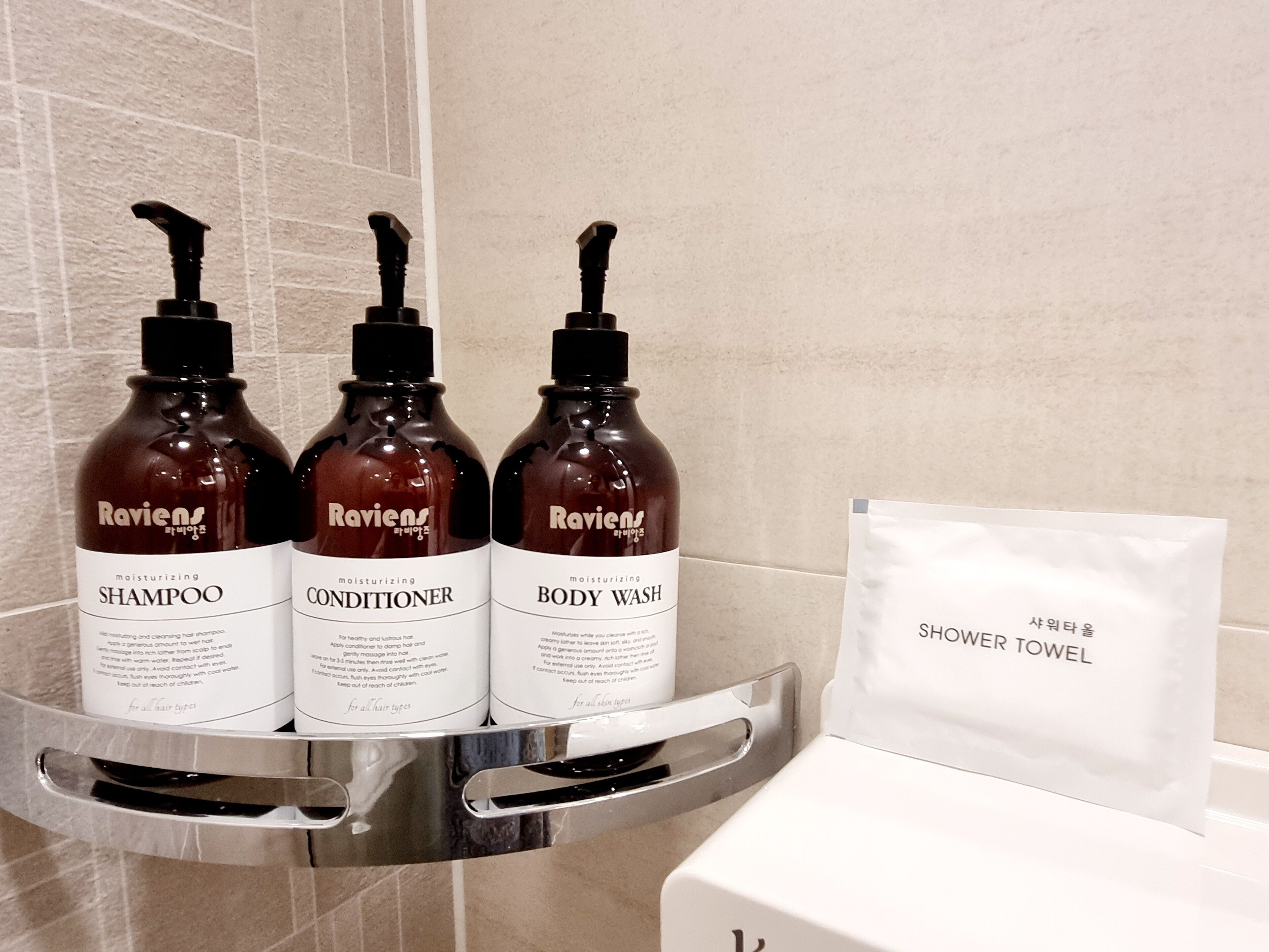 A bathroom shelf with three bottles of Ravien's hair care products and a white shower towel.