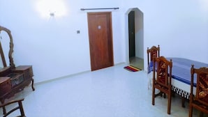 A room with a wooden door, a small table with chairs, and a wall-mounted light fixture. - Volga Guest House (Weligama)