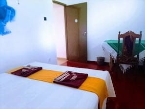 A hotel room with a bed, a wooden chair, a table with a green tablecloth, and a door. - Volga Guest House (Weligama)