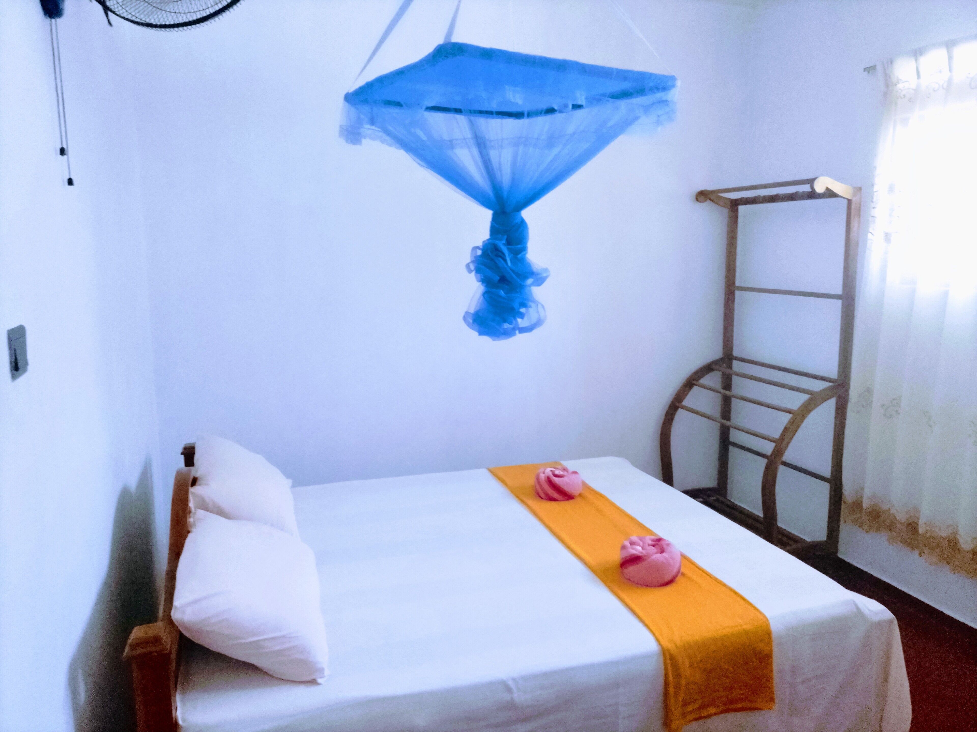 A single bed with white bedding and a yellow accent, a blue mosquito net, a wooden ladder, and a white wall.