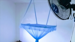 A bed with a mosquito net, a fan, and a wooden headboard. - Volga Guest House (Weligama)