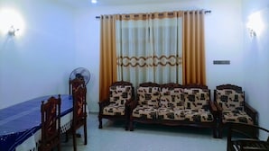 A living room with a dining table, chairs, a sofa set, a standing fan, and curtains. - Volga Guest House (Weligama)