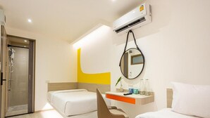 Habitación de hotel con una cama, un escritorio con una silla, un espejo y un equipo de aire acondicionado.