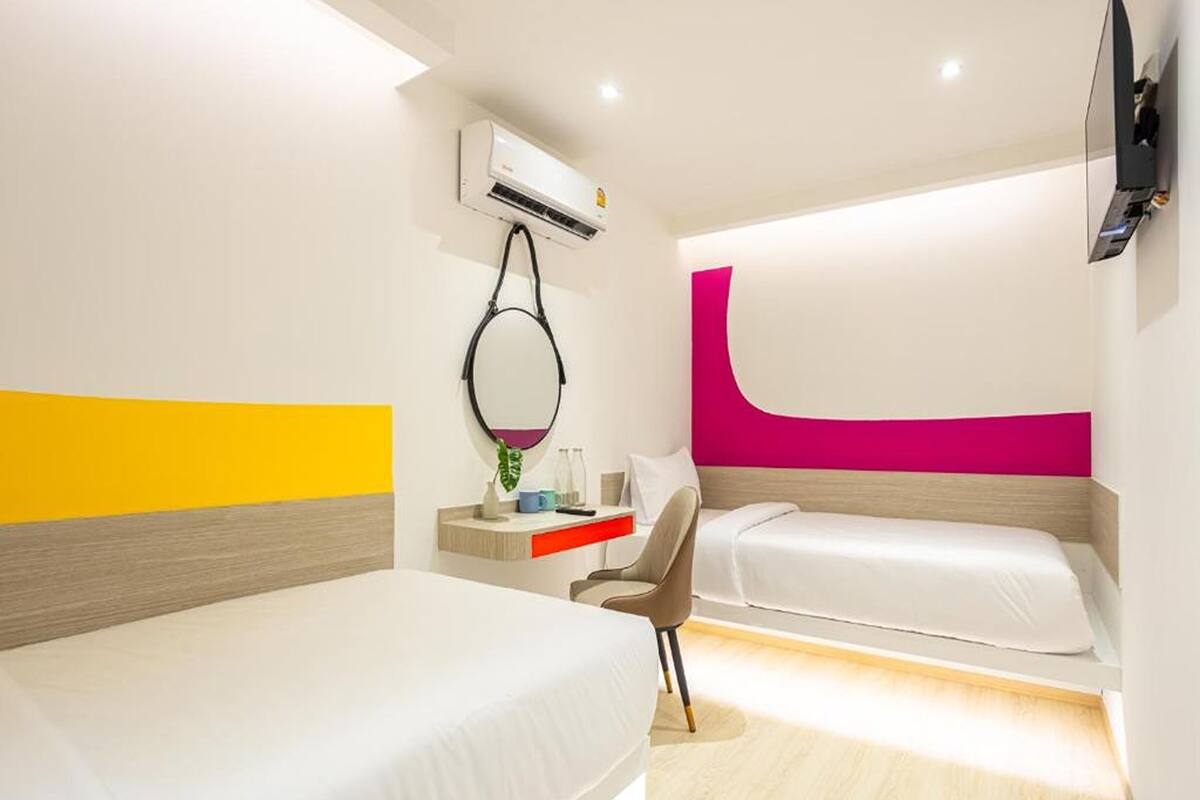 Quarto de hotel com duas camas, uma escrivaninha com cadeira, televisão e aparelho de ar condicionado.