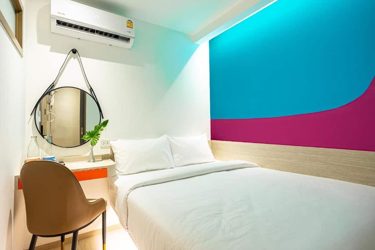 Quarto de hotel moderno com uma cama, uma escrivaninha com cadeira, um espelho redondo e um aparelho de ar condicionado.