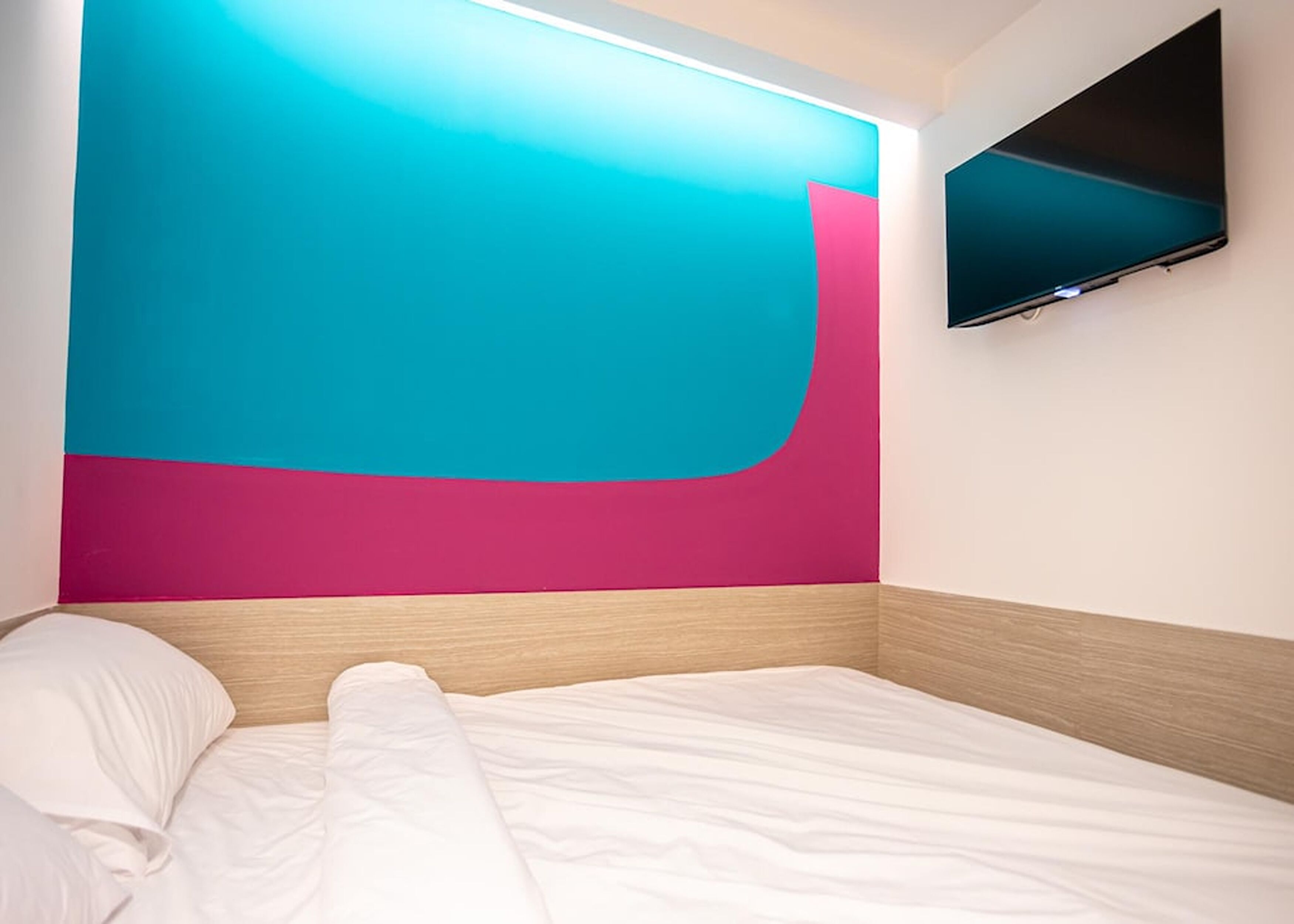 A modern hotel room with a large bed, a flat-screen TV mounted on the wall, and a vibrant wall design.