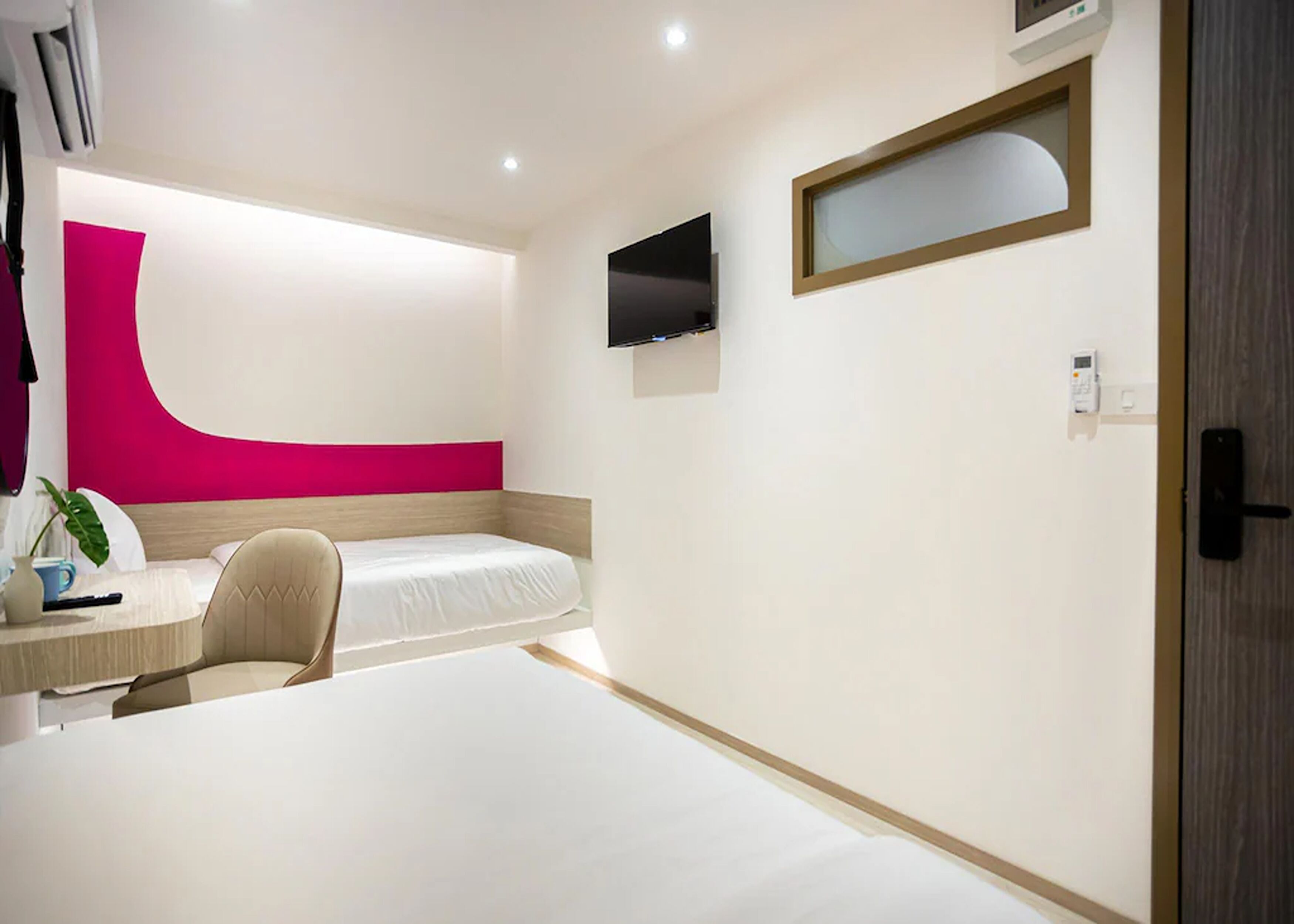 A modern hotel room with a bed, a desk, a chair, a TV, and a window.