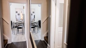 A hallway leading to a dining area with a table set for four, a clock on the wall, and a door on the right. - 4 Bed House, Sleeps 9, Free Parking (Stoke-on-Trent)