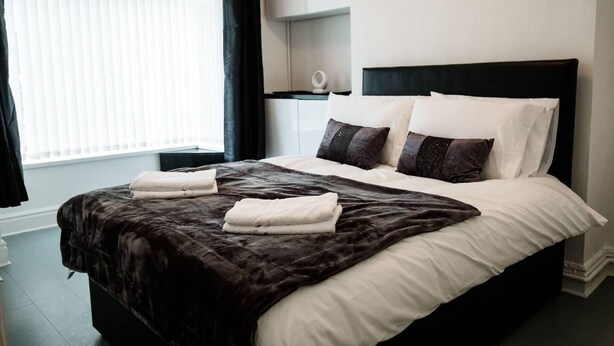 A neatly made bed with a dark headboard, white linens, and two folded towels. - 4 Bed House, Sleeps 9, Free Parking (Stoke-on-Trent)