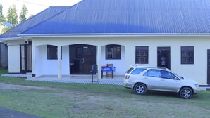 A two-story building with a blue roof, a covered porch, and a parked car. - Rainbow hotel-annex (Bundibugyo)