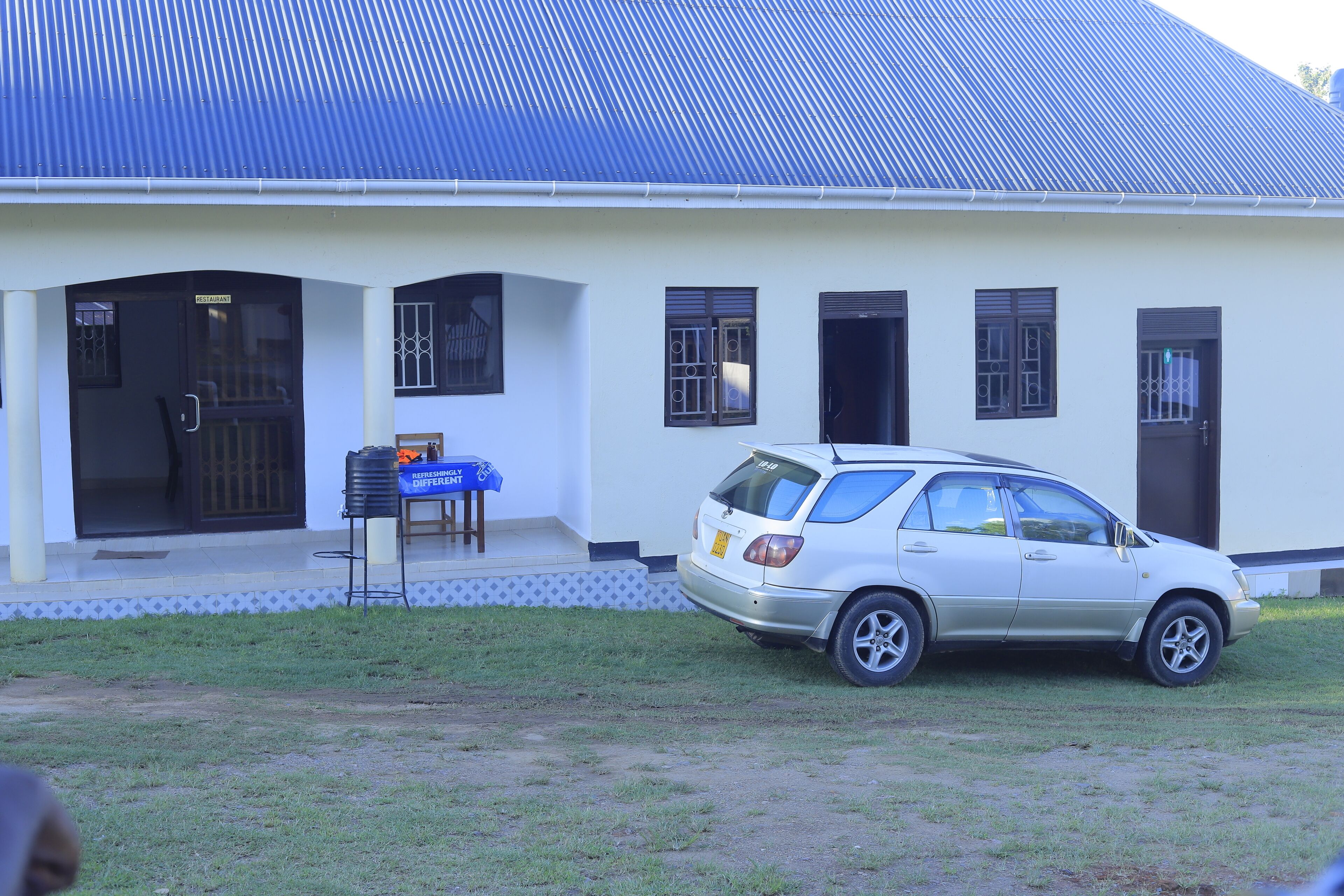 A white building with a blue roof, a parked car, and a signboard.