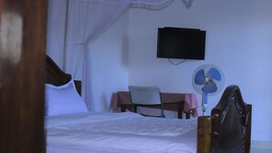 A bedroom with a bed, a desk, a chair, a TV, and a fan. - Rainbow hotel-annex (Bundibugyo)