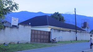 A guest house with a large garage, a motorcycle parked outside, and a mountain backdrop. - Rainbow hotel-annex (Bundibugyo)