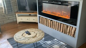 Una sala de estar moderna con una pared de piedra, un televisor, una chimenea y una mesa de centro redonda de madera.