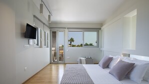 A modern bedroom with a large bed, a TV mounted on the wall, and a view of the outdoors through the window. - Villa Kymo by Thines Villas (Lefkada)