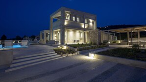 A modern two-story building with a pool area, outdoor seating, and a well-lit entrance. - Villa Kymo by Thines Villas (Lefkada)