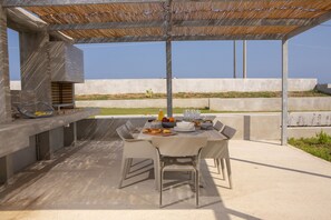 An outdoor patio with a table set for dining, a grill, and a view of the landscape. - Villa Kymo by Thines Villas (Lefkada)