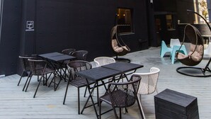 An outdoor seating area with tables and chairs, string lights, and a building in the background.