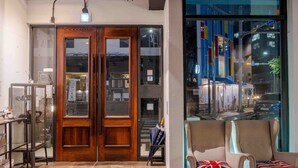 A hotel lobby with a wooden door, a reception desk, and two armchairs with pillows.