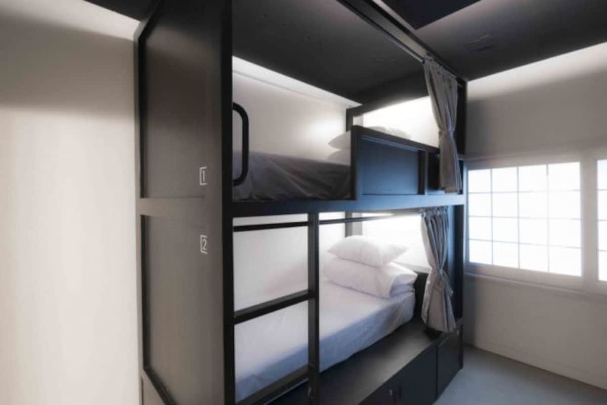 A bunk bed room with a window, curtains, and a small shelf.