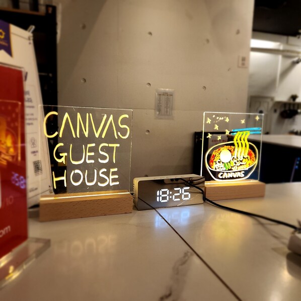 A digital clock displaying 18:26, a neon sign reading "CANVAS GUEST HOUSE," and a neon sign with a food illustration. - Canvas Black Guesthouse (Busan)