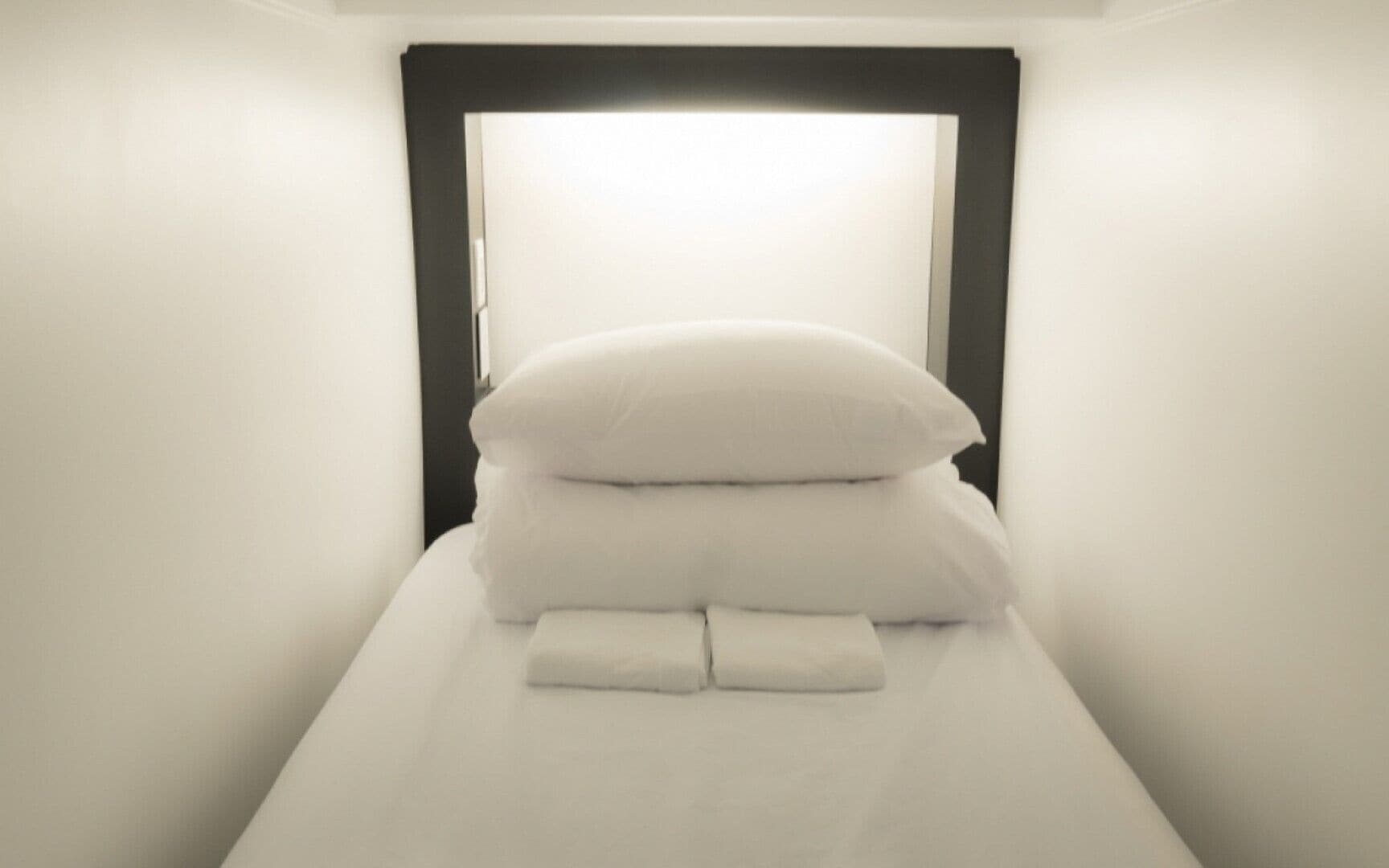 Ein ordentlich bezogenes Bett mit weißen Leinen und Kissen in einem Zimmer mit weißen Wänden und einem dunklen Kopfteil.