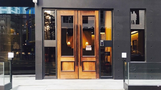 A building entrance with a double wooden door, a glass window, and a small sign above the door.