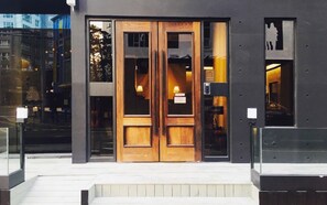 A building entrance with a double wooden door, a glass window, and a small sign above the door.