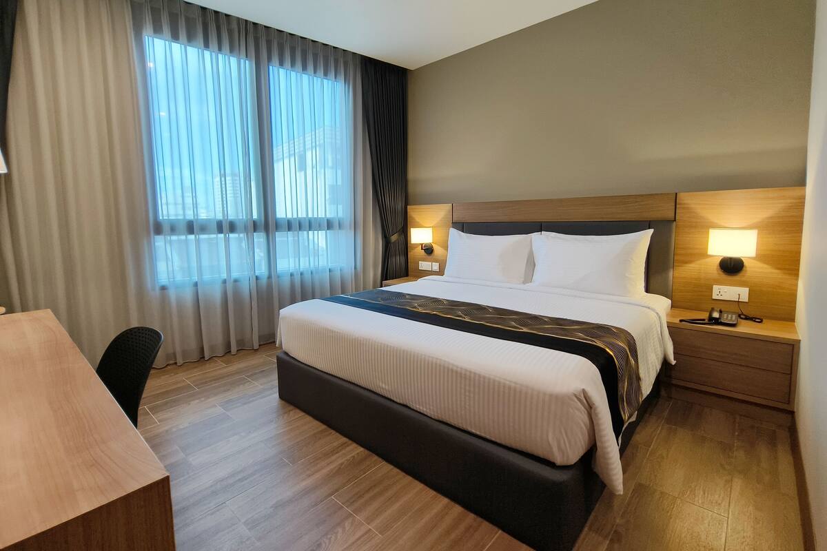 A hotel room with a large bed, bedside lamps, a desk, and a view of the city through the window.