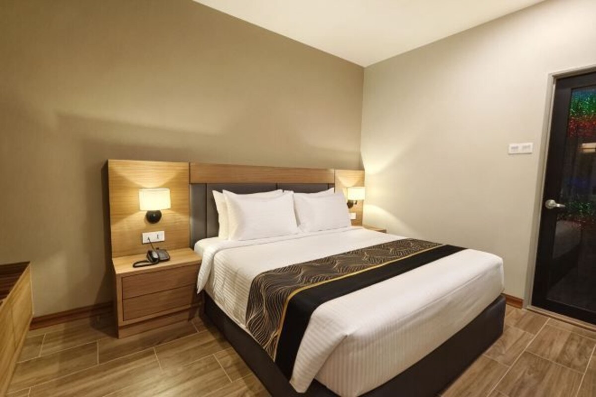 A hotel room with a large bed, bedside lamps, a nightstand, and a door with a glass panel.