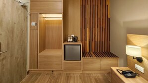A compact hotel room with a wooden wardrobe, a small minibar, a desk with a telephone, and a wall-mounted lamp. - ZOOM HOTEL (George Town)