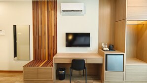 A modern room with a wooden desk, a TV, a mini-fridge, and a built-in bench. - ZOOM HOTEL (George Town)