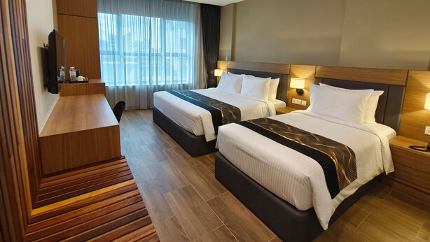 A hotel room with two beds, a wooden desk, a flat-screen TV, and a large window with curtains. - ZOOM HOTEL (George Town)