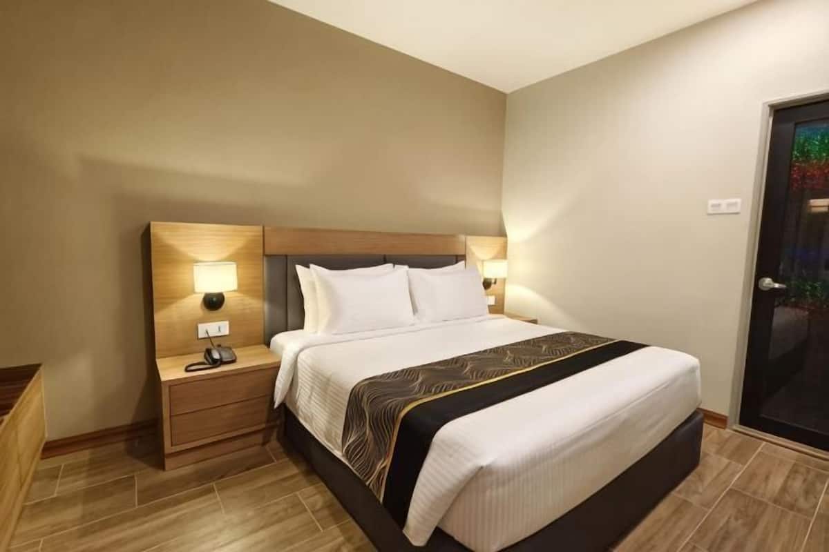 A hotel room with a large bed, bedside lamps, a nightstand, and a door with a glass panel.