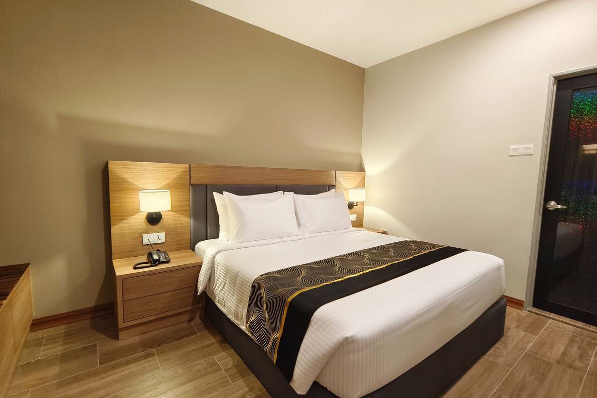 A hotel room with a bed, bedside tables, lamps, and a door.