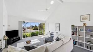 A modern living room with a large TV, a sofa, a coffee table, and a bookshelf. - Three Bedroom House with Ocean Views (Torquay)