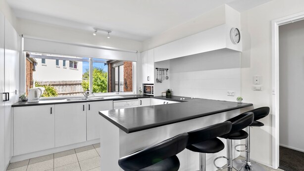 A modern kitchen with white cabinets, a black countertop, and a bar stool area. - Three Bedroom House with Ocean Views (Torquay)