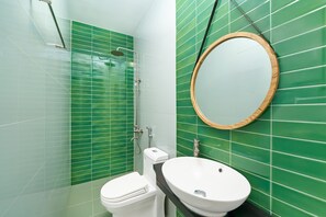 A bathroom with green tiles, a white toilet, a white sink, and a shower with a handheld showerhead. - Seven A Hotel (Xuan Huong - Da Lat)