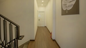 A hallway with a wooden floor, a white door at the end, and a fire extinguisher on the right. - Seven A Hotel (Xuan Huong - Da Lat)