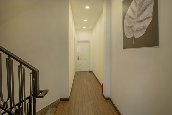 A hallway with a wooden floor, a white door at the end, and a fire extinguisher on the right.