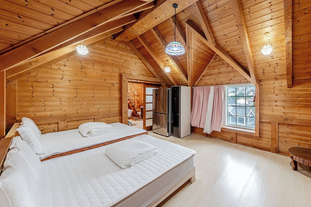 Eine Holzhütte mit einem Bett, einem Kühlschrank, einem Fenster und einer Tür zu einem Badezimmer.