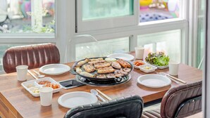 A dining table with a variety of dishes, including grilled meat, vegetables, and side dishes, set in a room with a view of the outdoors. - Gyeongju Liune Kids Pool Villa Pension (Gyeongju)