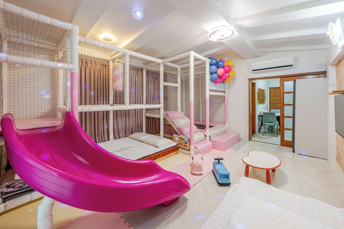 Ein Spielbereich mit einer rosa Rutsche, einem Spielkäfig und einem kleinen Tisch mit Spielzeug.