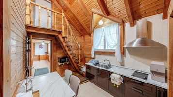 Interior de una cabaña de madera con cocina, comedor y una escalera que sube a un nivel superior.
