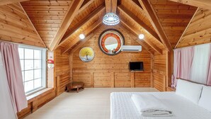 A wooden cabin bedroom with a bed, a TV, a circular mirror, and a window with curtains. - Gyeongju Liune Kids Pool Villa Pension (Gyeongju)