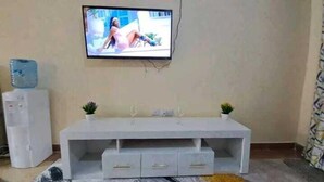 Un salon avec un téléviseur à écran plat fixé au mur, un meuble de rangement blanc doté de tiroirs et une petite plante en pot posée sur le meuble.