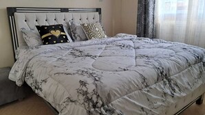 Un lit avec une couette à motifs de marbre, une tête de lit capitonnée et plusieurs oreillers, dont un orné d’un motif en forme de cœur.