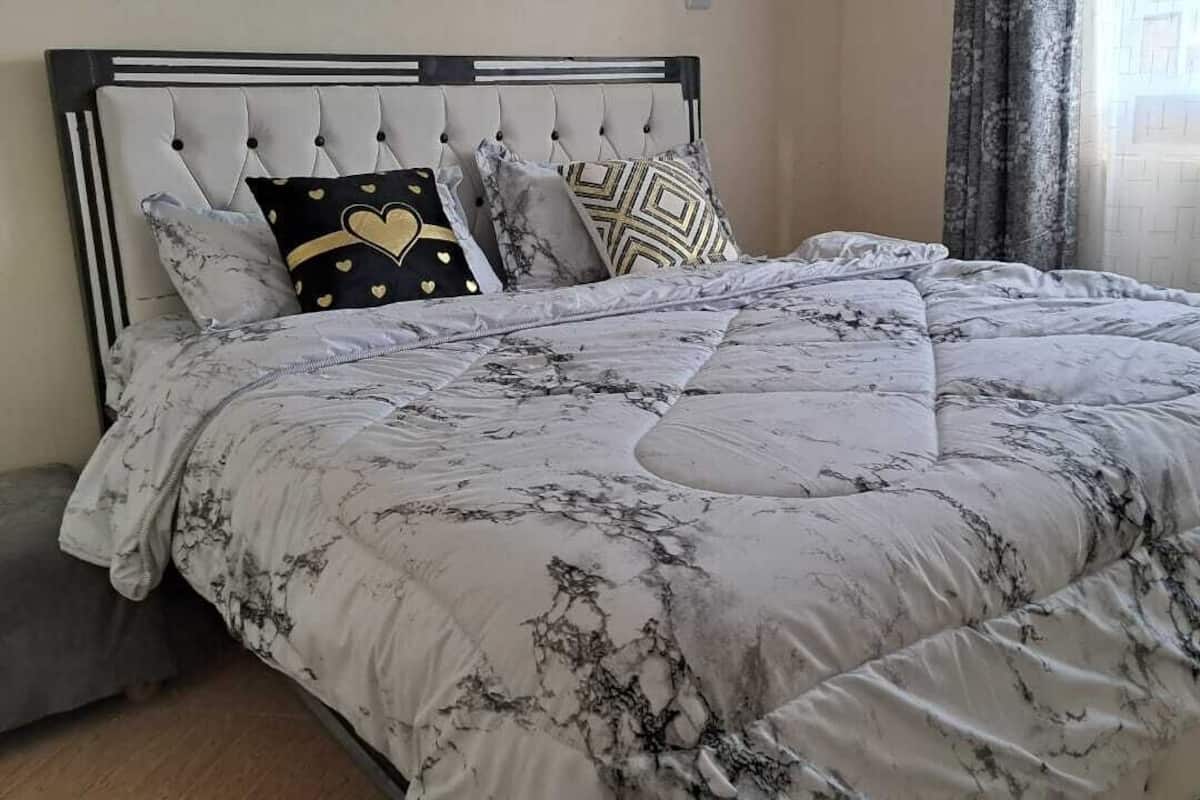 A bed with a marble-patterned duvet, a tufted headboard, and several pillows, including one with a heart design.