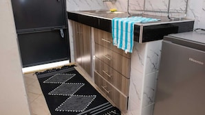 Une cuisine compacte avec un réfrigérateur noir, des armoires en bois, un pare-feu en marbre et un tapis à motifs noir et blanc.